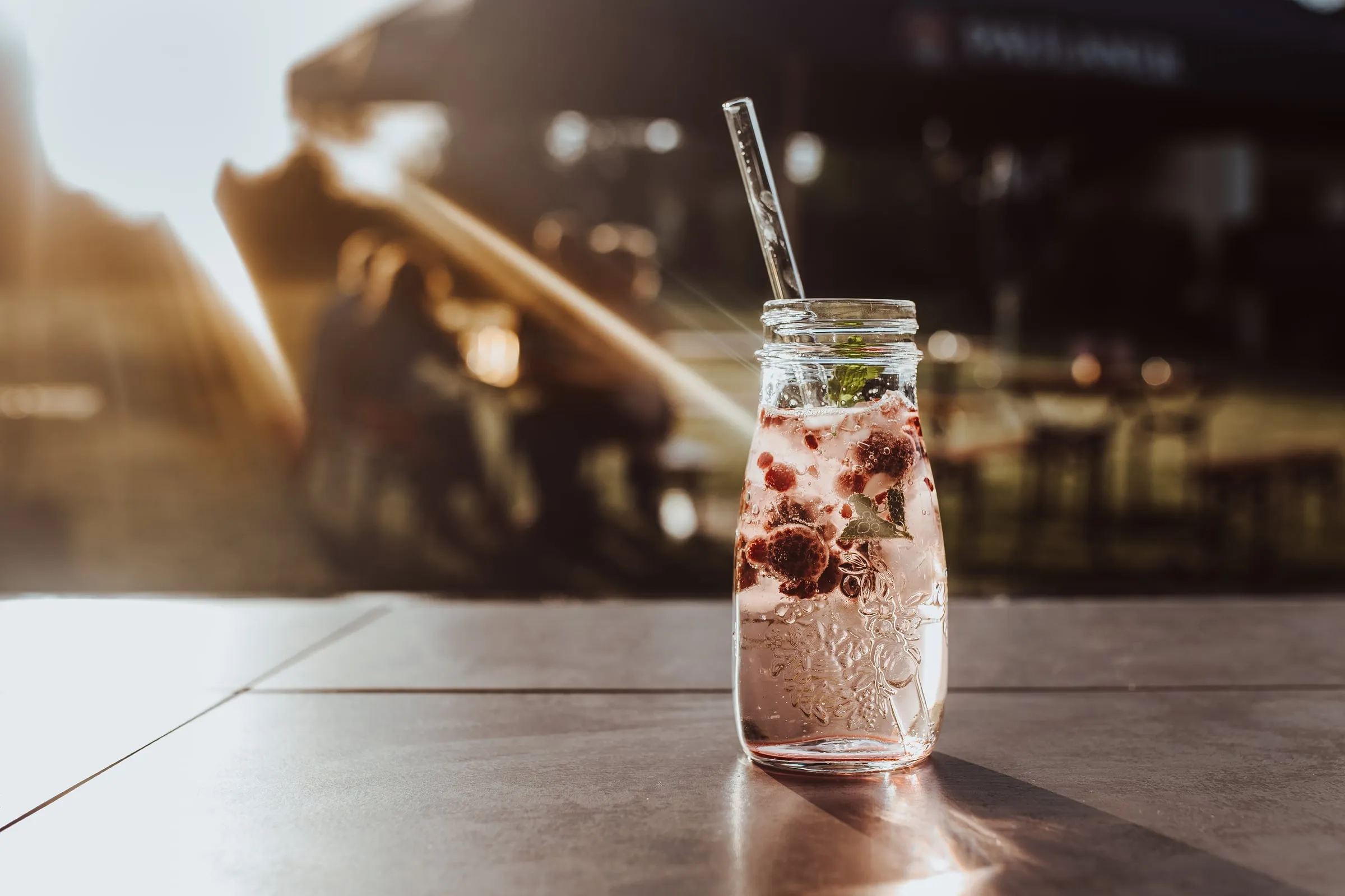 Beerengetränk in einer Glasflasche mit Strohhalm im Gegenlicht auf einem Tisch im Biergarten