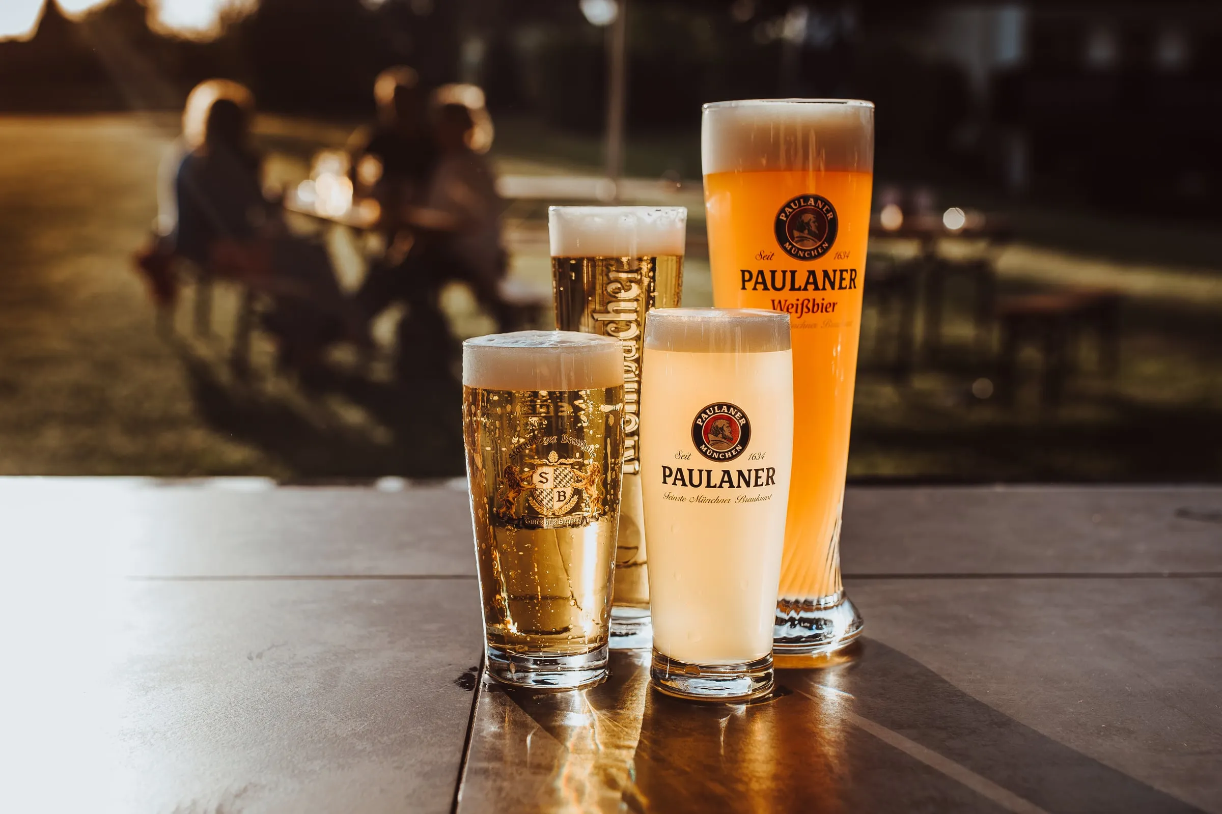 Vier gefüllte Biergläser auf einem Tisch im Abendlicht