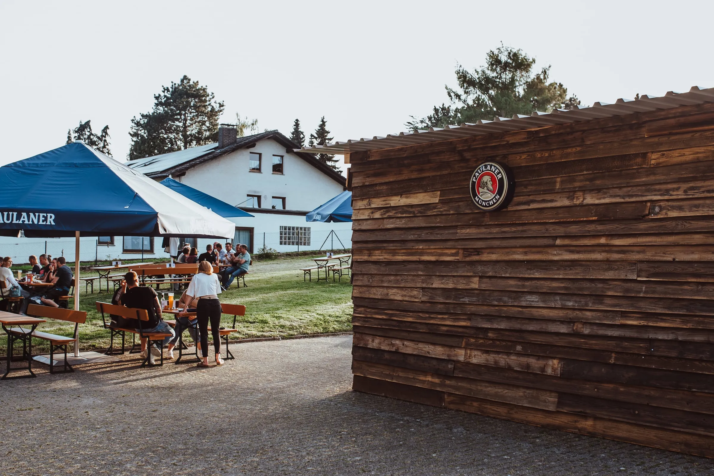 Außenbereich des Borchener Biergartens mit Sonnenschirm, Bierbänken und Holzhütte